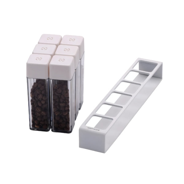 Six white Normcore Coffee Bean Cellars V2 tubes filled with coffee beans beside the empty white six-slot stand